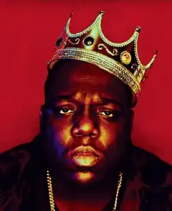Photograph of Wallace staring at the camera, wearing a crown in a red background