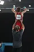 Gymnast graps the apparatus (here: horizontal bar), afterwards the coach steps back