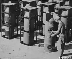 Black and white photo of man and a large number of cylindrical objects