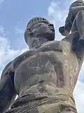 The central figure of the monument depicts a muscular man holding a child aloft with one hand while stretching the other arm outward