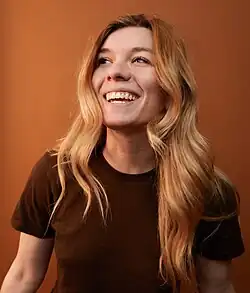 Portrait photograph of Rauwerda, a young, blonde, white woman, looking at the top-left, smiling