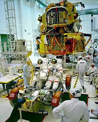 Schmitt, (left), Cernan, (right) in a training LRV, with the Lunar Landing Module in the background.