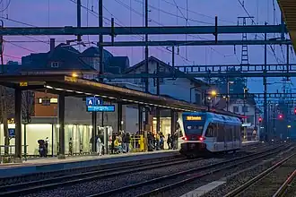 White train on tracks next to side platform in low light