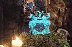 A furry blue toy with a flower crown sitting atop a shrine.