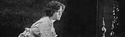 Black and white film still showing a woman in elegant dress