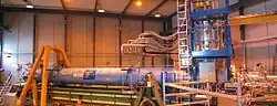 A warehouse interior containing a long blue cylinder surrounded by scaffolding and plumbing.