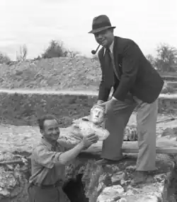 Black and white photo of two men holding a statuette over a hole.