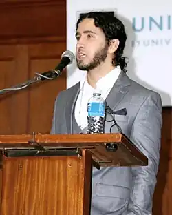 a man a suit standing at a podium with a microphone