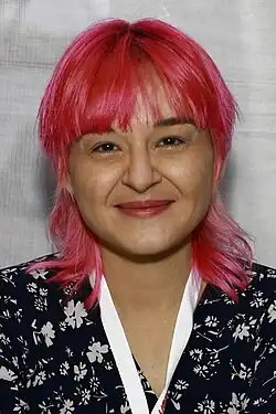 Portrait of Darcie Little Badger, a young Apache woman wearing a bandana, standing behind a wall of hanging cloths