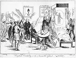 A small audience of people surround a bed, in which two children lie. A ghostly figure hovers above the children, a hammer in one hand. One man looks under the bed, with a candle. Speech bubbles are visible from each member of the audience. To the right of the image, several women are engaged in prayer.