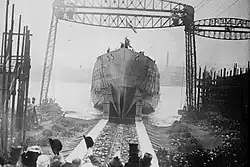 A black and white photograph showing a ship's hull with no superstructure sliding down a slipway into a waterway