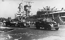 HNLMS De Ruyter moored in Surabaya port. KNIL mechanized forces are with a Braat Overvalwagen armored car behind the rest.