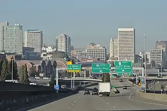 A freeway leading towards a cluster of high-rise buildings, parallel to a railroad