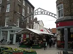 A metal sign affixed between two buildings, with a wide street between the two buildings