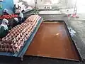 Kolhapur jaggery in semi-liquid form filled in the "Vafaa" rectangular section. Later will be transferred into the 1 Kg containers with white cloth placed inside it for making Jaggery blocks (Dheps)