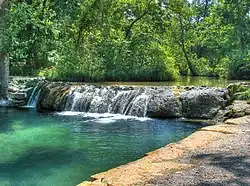 Small waterfall along a river's path with trees shading it