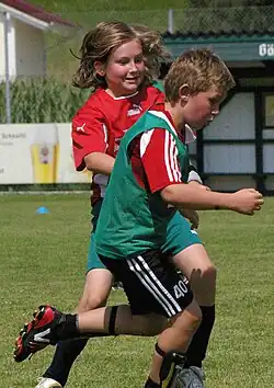 A boy and a girl chase a soccer ball