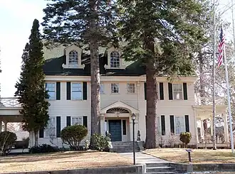 Photograph of the front of a stately three-story Georgian Revival house, with three large dormers and porches at both right and left ends of the house.