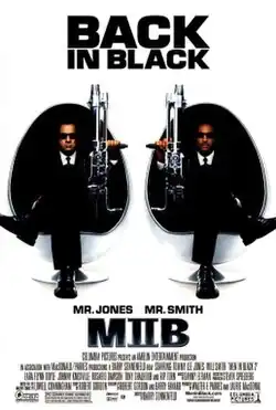 Two men in black men, sitting in egg shaped chairs, holding large guns