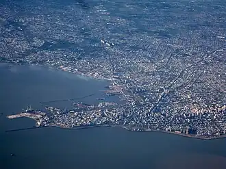 View of coastal city with higher-rise buildings and a port in the foreground and lower-rise buildings further away