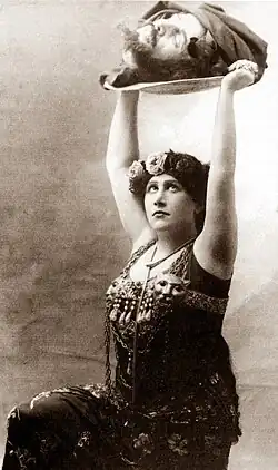 young woman in ancient middle-eastern costume holding a tray on which is a severed male human head