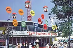 A single-story, glass-fronted building with a sign saying "Les Poupées de Paris" (The Dolls of Paris).