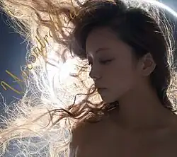 A blue-tinted close-up face shot of a woman, with long hair being windswept to her right. In the background is an extreme close-up of an annular solar eclipse.