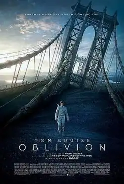 Tom Cruise wearing his space suit, walking along the desolate land with the ruined Manhattan Bridge behind him.
