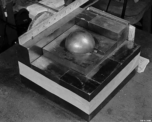A square base of metal blocks, with a smaller square of metal on the top in the center, a Cooper block (the "core") contained in its center. A ruler along one side of the base shows roughly 10.5 inches (270&nbsp;mm) square.