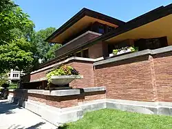 The facade of the house as seen from 58th Street. The house has a brick facade with stone and concrete decorations. There is an overhanging cantilevered roof at the center.