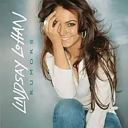 A red-headed woman poses with a hand covering her left eye front of a silver-colored background. The words "Lindsay Lohan" are written in white and are flipped to the vertical position, as is the word "Rumors" written in navy blue.