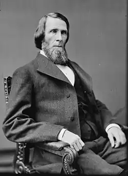 Black and white photograph of a bearded man seated in a chair facing the camera