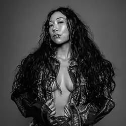 A black and white photograph of Sasami. Her head is titled to the right and a red drop of blood is running down her lip. Sasami wears a leather jacket cover her bare chest.