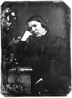 early photograph of a middle-aged white man, clean shaven, seated, leaning on the hand of his right arm, of which the elbow is on the adjacent table
