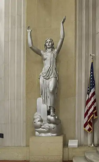 woman, nude above waist, raises both arms above head.