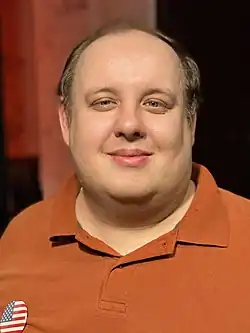 Steven Pruitt in 2022. He is a middle-aged man with dark blond hair wearing an orange collar shirt.