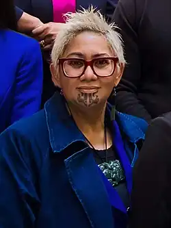 Kemp looking at the camera wearing a blue jacket with tattoos on her chin