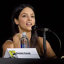 Tala Ashe sitting down behind a name plate reading Dominic Purcell and a microphone