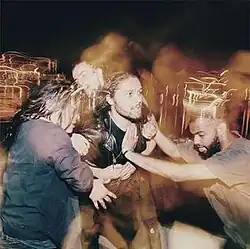 A motion-blurred photograph of David Le'aupepe being held back by his three bandmates.