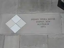 Four square tiles embedded in the facade, arranged in a diamond pattern with the top and bottom tiles lighter in color than the right and left tiles