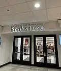 Two sets of double doors with large glass windows, slightly recessed into the wall, below an overhang with lettering that reads "University of Minnesota Bookstore". On either side of the doors, on the wall before it recesses, is a television.