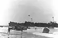 LST-344, (left) and LST-338 (right) unloading troops and supplies on the Gela invasion beaches in Sicily on "D-Day" 10 July 1943. Broached LCVP at right is from the Barnett&nbsp;(APA-5); the next LCVP to the left is from the Monrovia&nbsp;(APA-31).