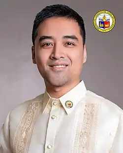Sotto during a public address in 2024 from a black office chair wearing a polo shirt with blue and white stripes and a lanyard