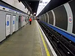 The interior of a building with a rounded ceiling, rounded walls, and a man wearing an orange jacket walking towards the back wall